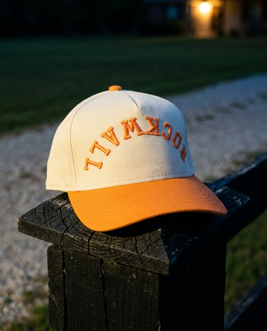 Rockwall upside down hat, cream crown with orange brim and orange embroidery, on a fence post at dusk in Rockwall Texas