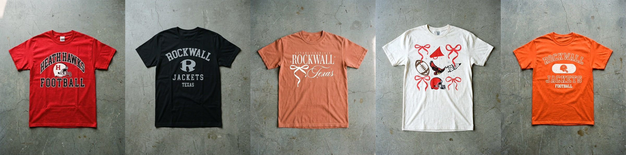 Five Pearl and Pennant spirit tees laid flat on concrete in a row, Heath Football Red Zone in red, Rockwall Arched Basic in black, Rockwall Bow So Cute in terracotta, Heath Spirit Checkered in natural and Rockwall Old School in orange