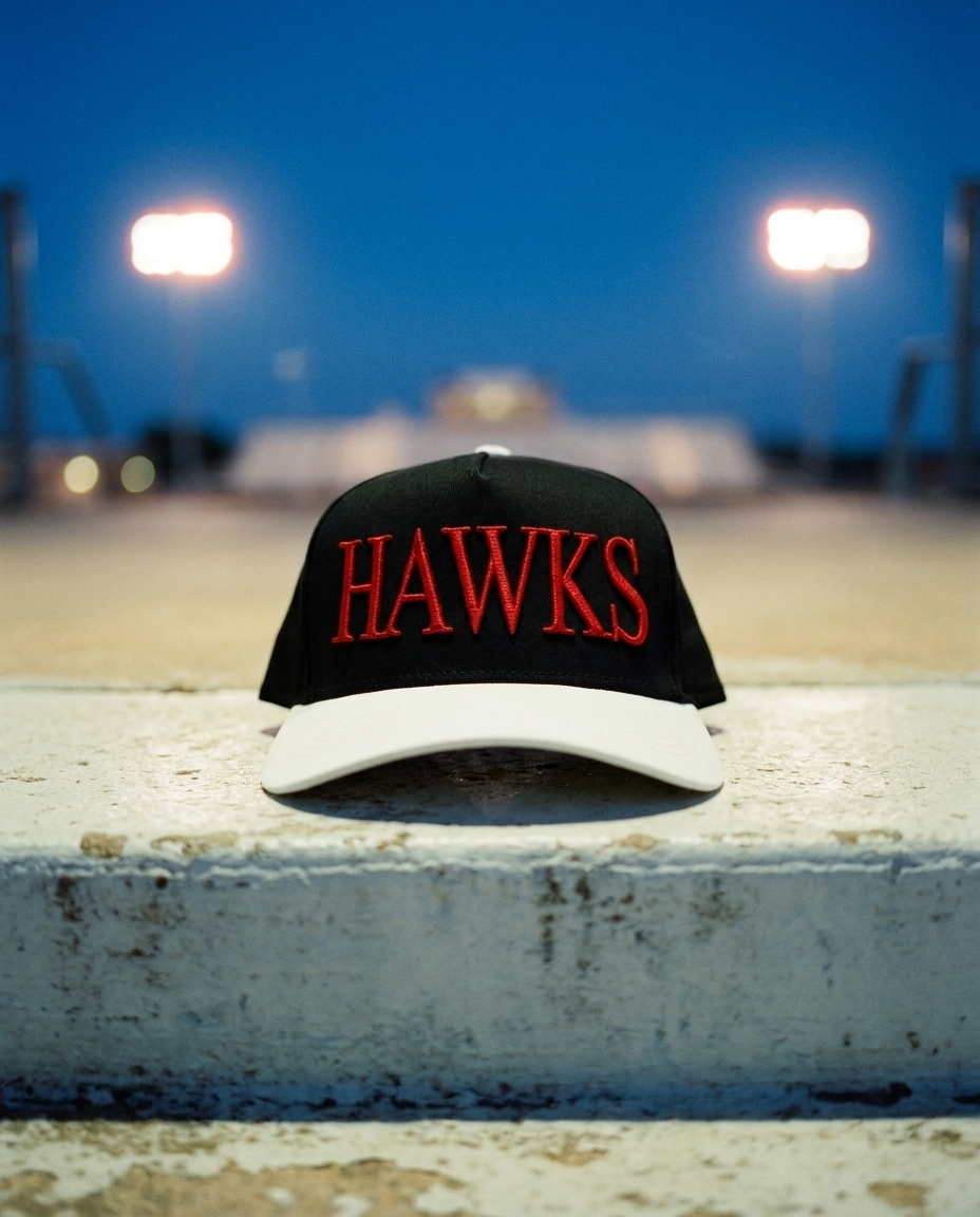 BKWHRD Heath Hawks big puff hat, black crown, white brim, red raised puff embroidery, on a stadium step at blue hour in Rockwall Texas