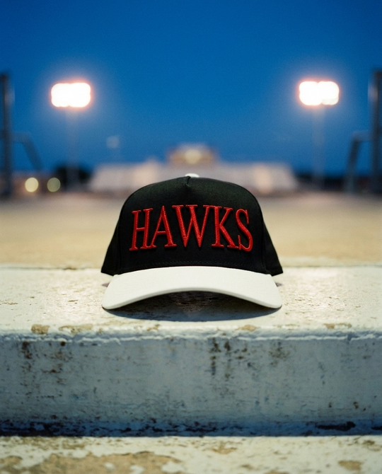 BKWHRD Heath Hawks big puff hat, black crown, white brim, red raised puff embroidery, on a stadium step at blue hour in Rockwall Texas
