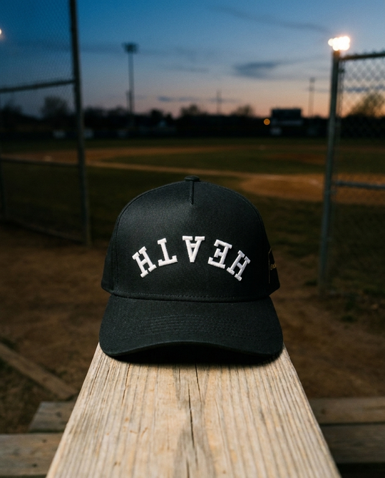 BKBKWH Heath upside down hat, black crown, black brim, white embroidery, on a baseball backstop rail at dusk in Rockwall Texas