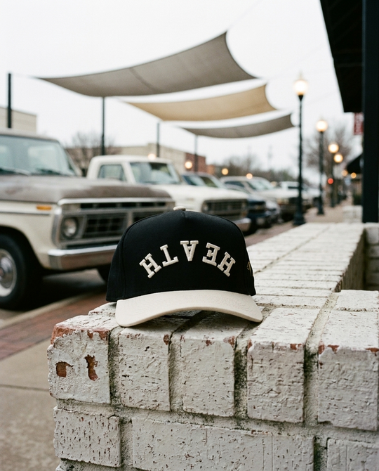 BKCRCR Heath upside down hat, black crown, cream brim, cream embroidery, on a brick ledge on the Rockwall square