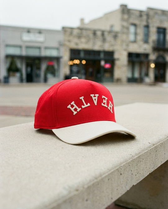 RDCRCR Heath upside down hat, red crown, cream brim, cream embroidery, on a bench on the Rockwall square
