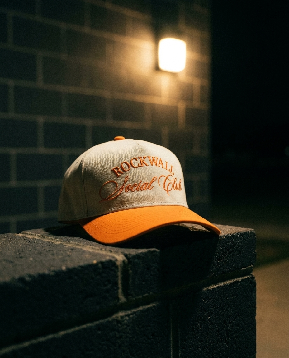 CROROR Rockwall Social Club hat, cream crown, orange brim, orange embroidery, by the field house at night in Rockwall Texas