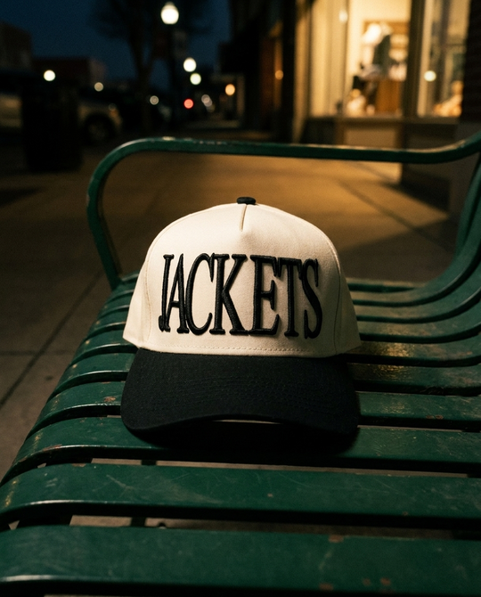 CRBKBK Rockwall Jackets big puff hat, cream crown, black brim, black raised puff embroidery, on a bench on the Rockwall square