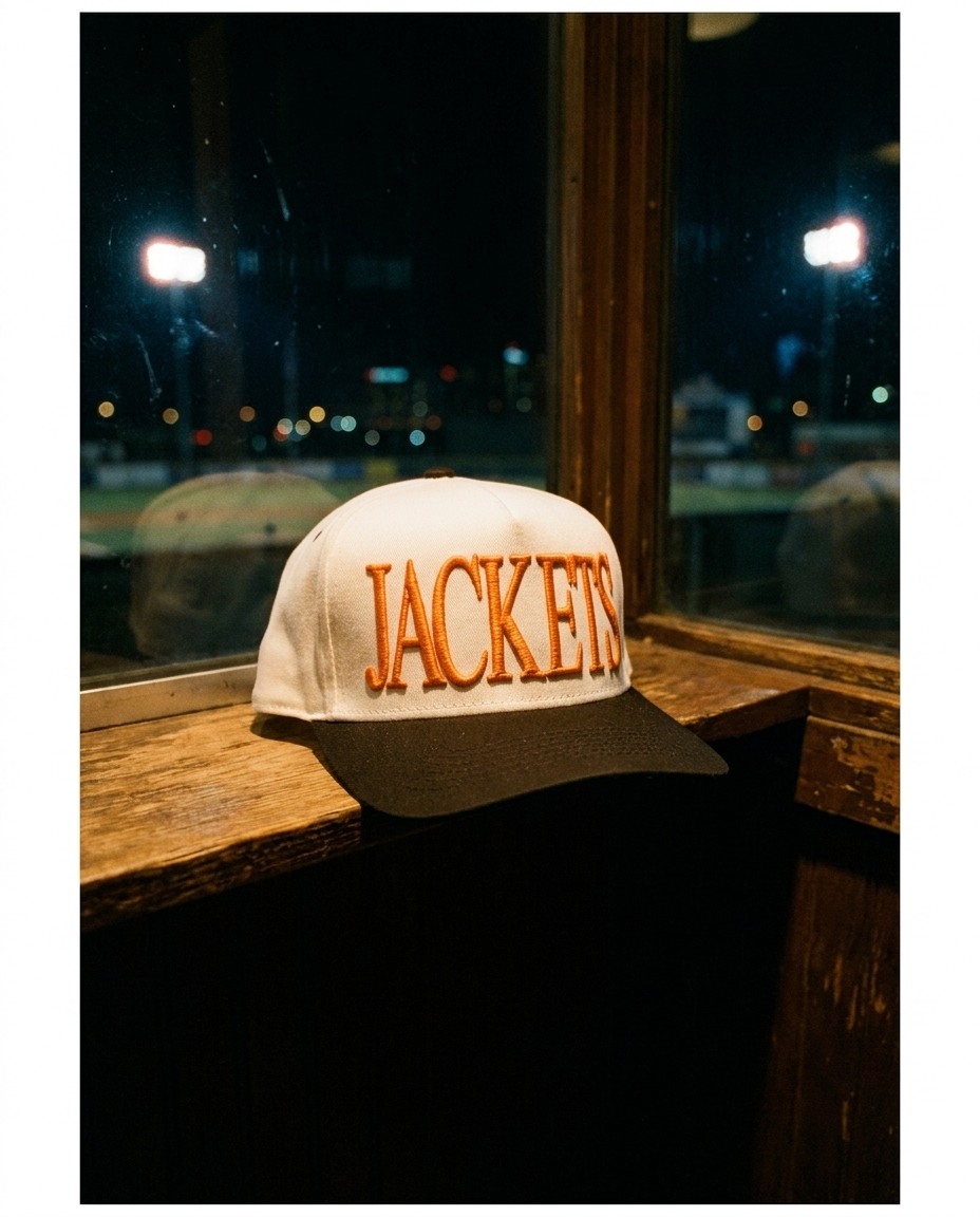 WHBKOR Rockwall Jackets big puff hat, white crown, black brim, orange raised puff embroidery, on a windowsill at night in Rockwall Texas