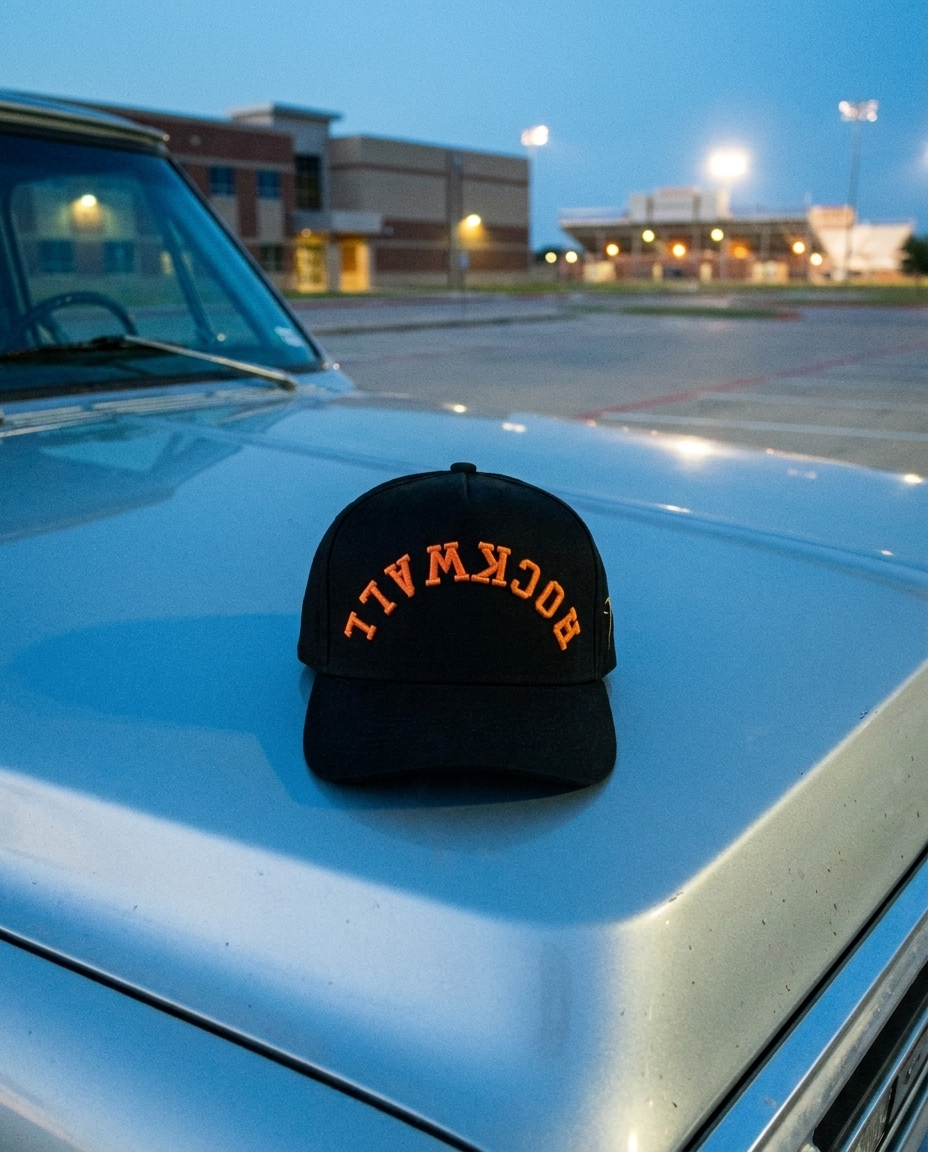 BKBKOR Rockwall upside down hat, black crown, black brim, orange embroidery, on a truck hood at blue hour in Rockwall Texas