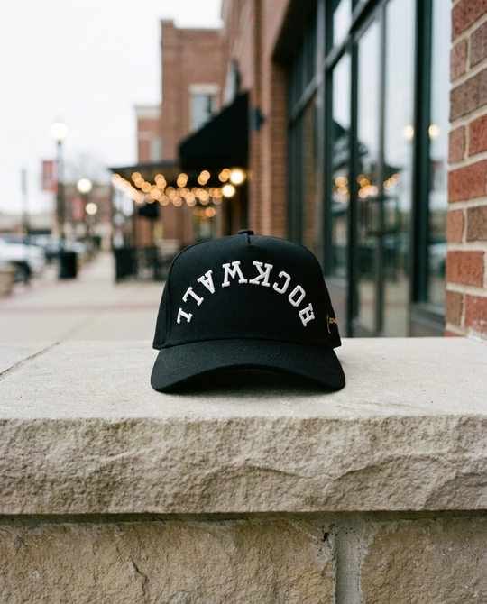 BKBKWH Rockwall upside down hat, black crown, black brim, white embroidery, on a limestone sill on the Rockwall square